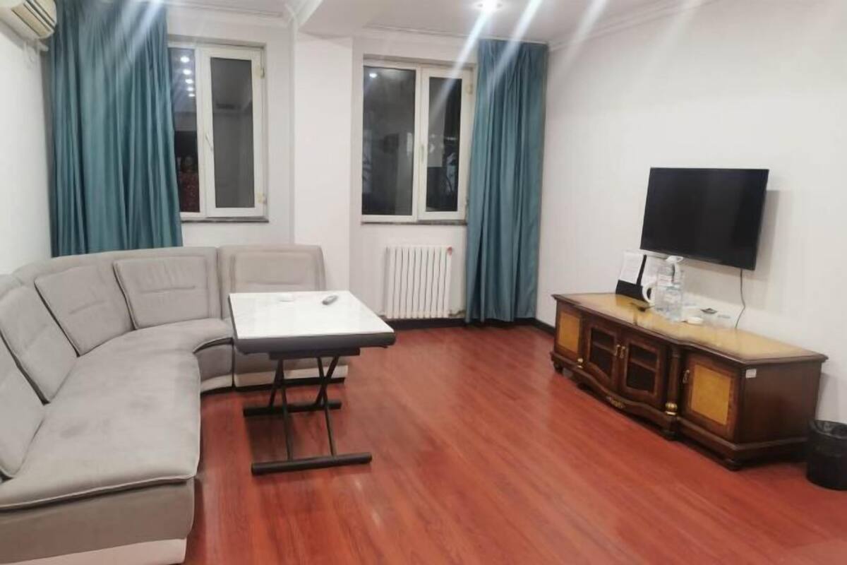 A living room with a sofa, a small table, a cabinet, a TV, and two windows with curtains.