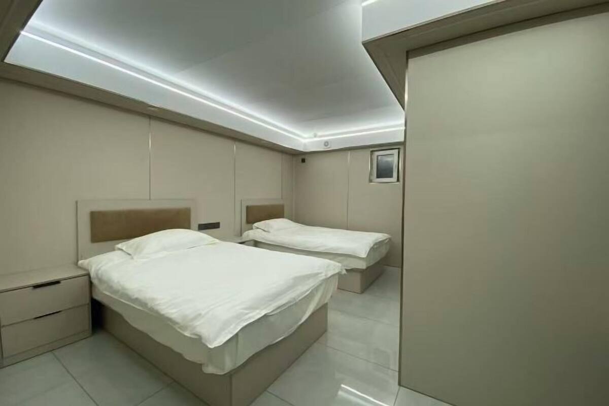 A modern hotel room with two beds, a wardrobe, and a small window.