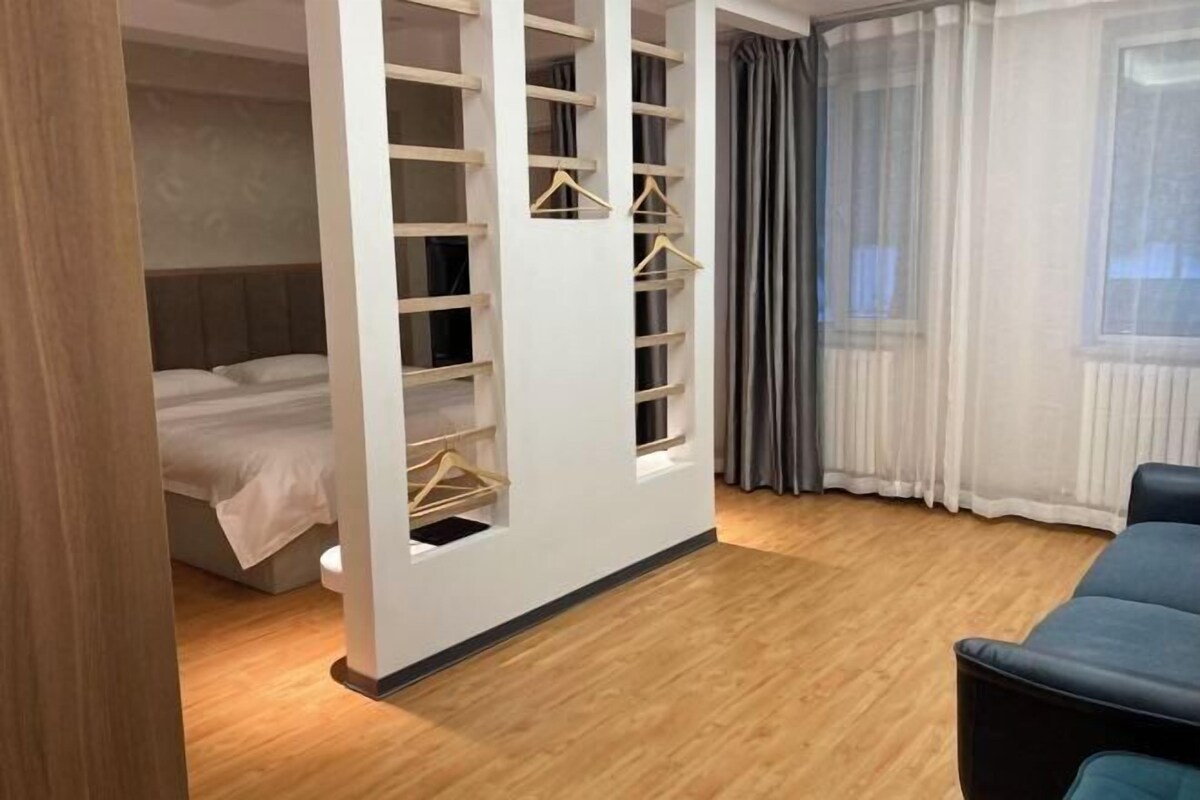 A bedroom with a bed, a wardrobe with hangers, a window with curtains, and a wooden floor.