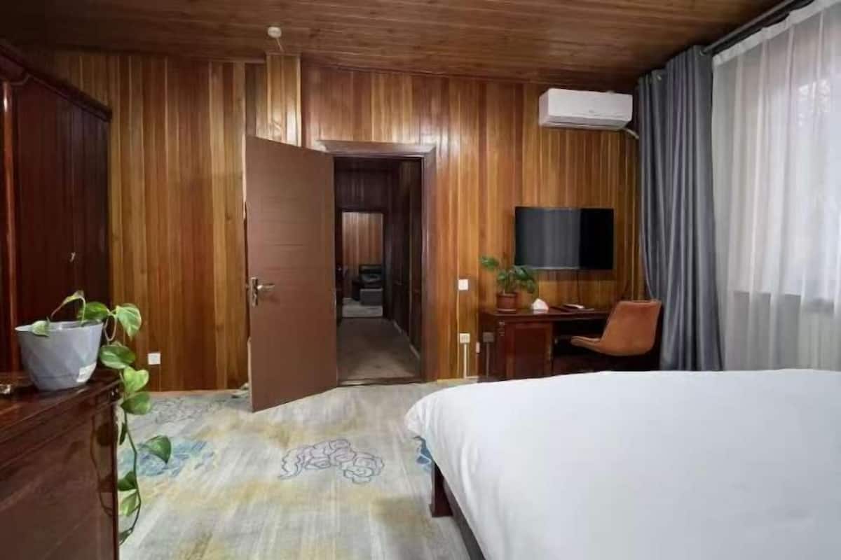 A hotel room with wooden paneling, a bed, a desk, a chair, a television, and a potted plant.