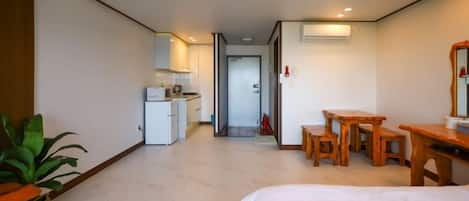 Quarto de hotel com cama, cozinha compacta, área de jantar com mesa e cadeiras, e planta em vaso.