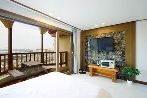 Hotelkamer met balkon, een bed, een televisie bevestigd aan een stenen muur en een tafeltje met een magnetron.