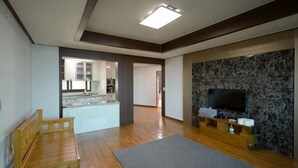 Un salón amplio con un banco de madera, un televisor de pantalla plana montado en una pared de piedra y una cocina visible al fondo.