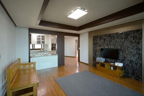 Un salón amplio con un banco de madera, un televisor de pantalla plana montado en una pared de piedra y una cocina visible al fondo.