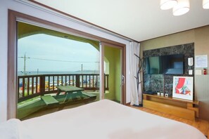 Een kamer met een bed, een televisie, een houten bankje en uitzicht op het strand.