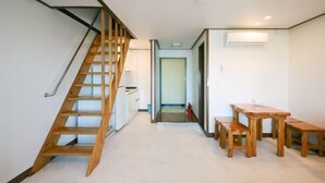 Una escalera que lleva a una plataforma, un comedor con mobiliario de madera y un pasillo con una puerta al final.