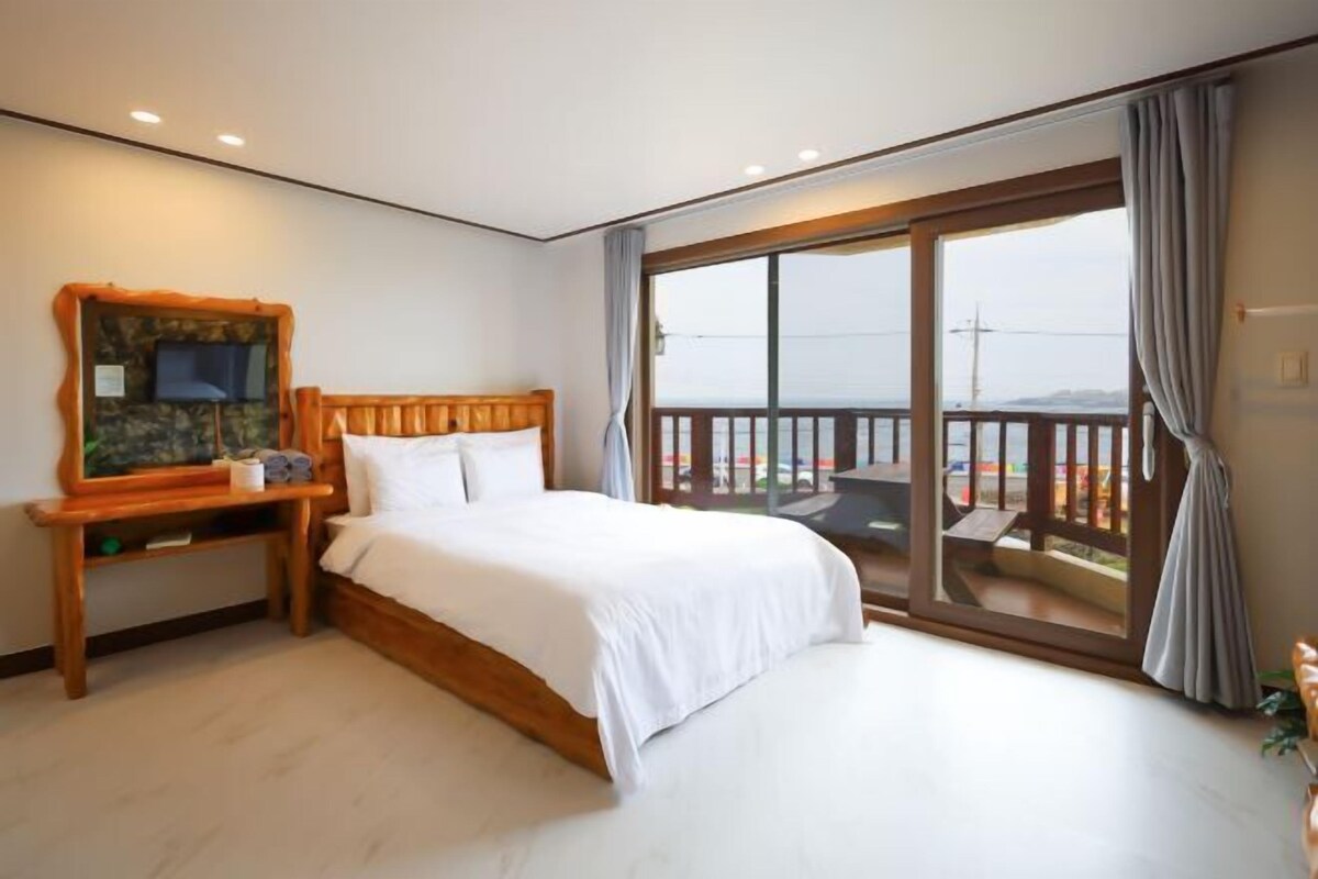 Een slaapkamer met een groot bed, een houten nachtkastje, een kleine televisie en een balkon met uitzicht.