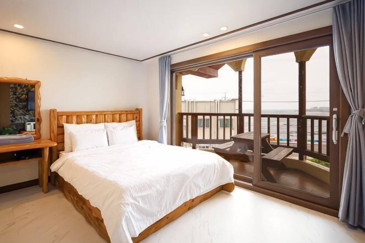 Un dormitorio con una cama grande, cabecera de madera, mesita de noche y vistas a un balcón con mobiliario exterior.