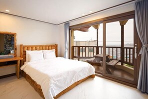 Un dormitorio con una cama grande, cabecera de madera, mesita de noche y vistas a un balcón con mobiliario exterior.
