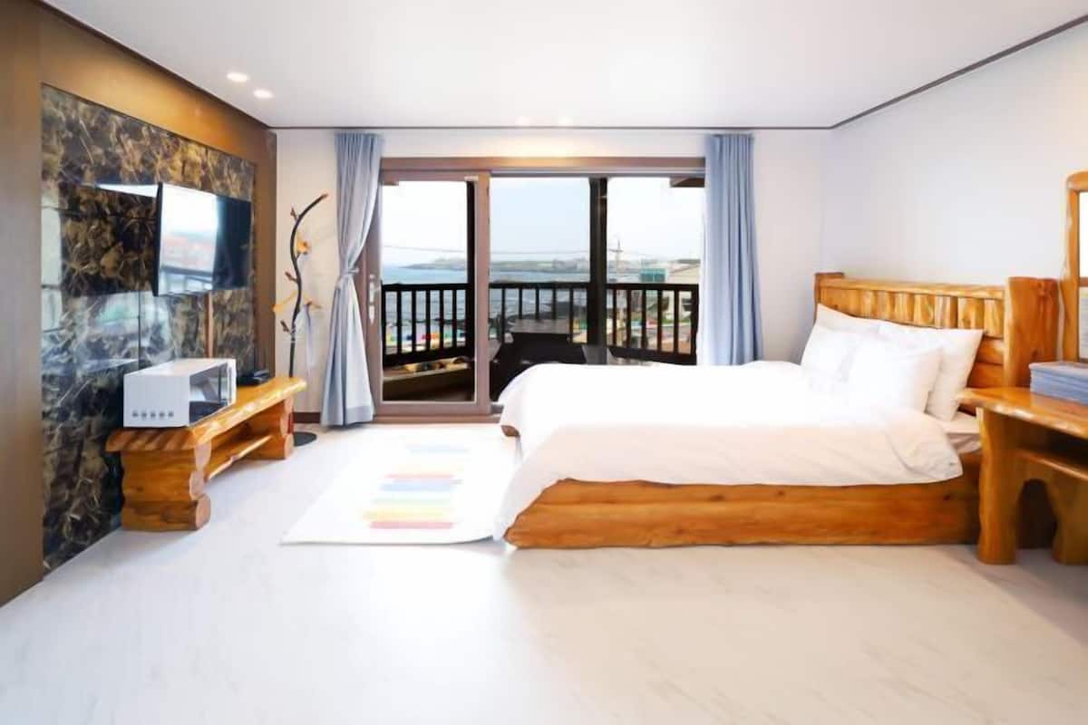 Un dormitorio con una cama grande, televisión, mesita de noche de madera y balcón con vistas.