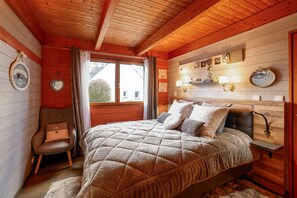 Ein gemütliches Schlafzimmer mit Holzboden, einem Bett mit gesteppter Bettdecke, einem Sessel mit Kissen und einem Fenster mit Vorhängen.