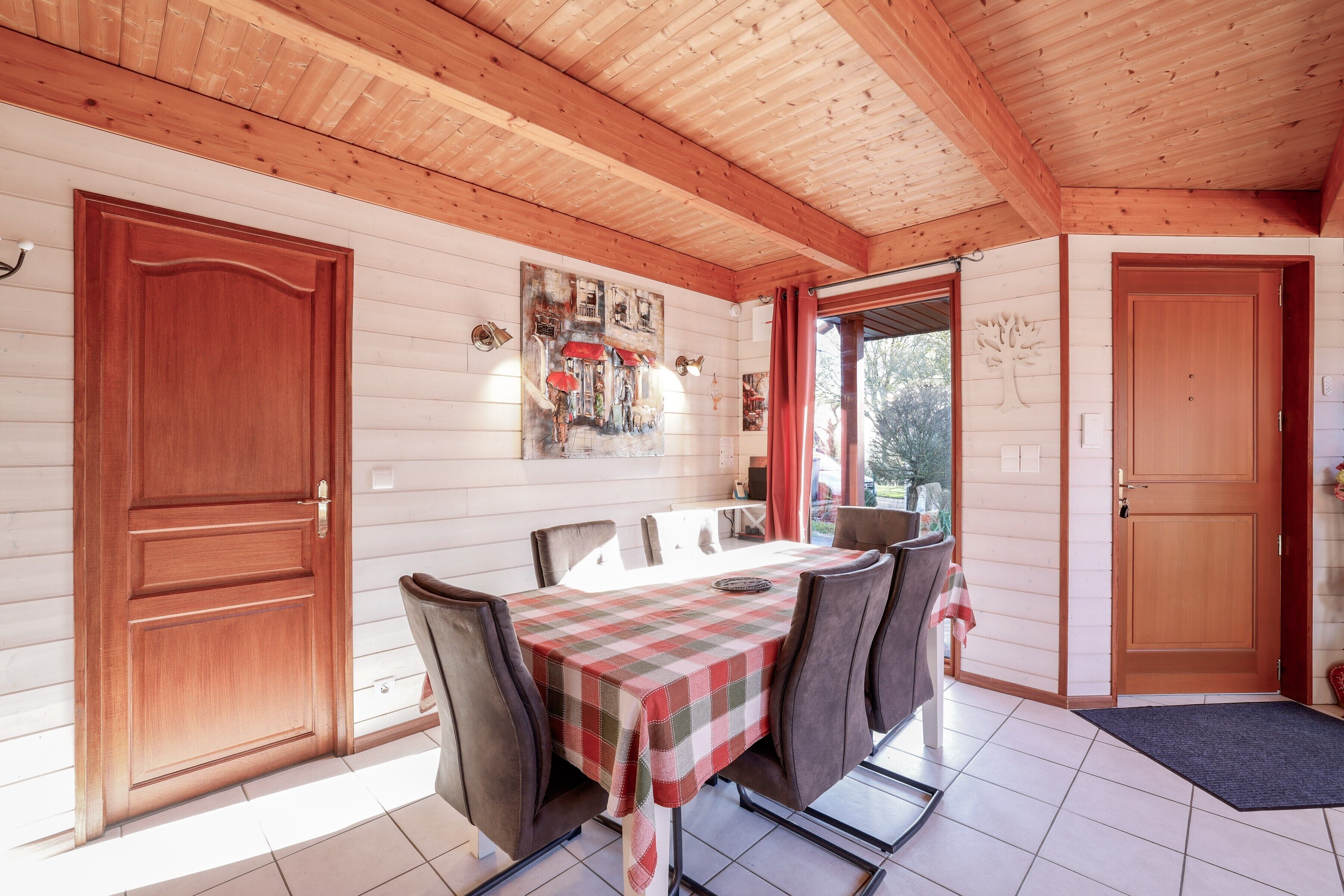 A wooden-paneled room with a dining table, chairs, and a door.