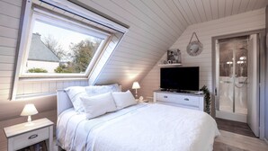 Et soveværelse med seng, fjernsyn, et natbord, lampe, et vindue og en bruseniche.