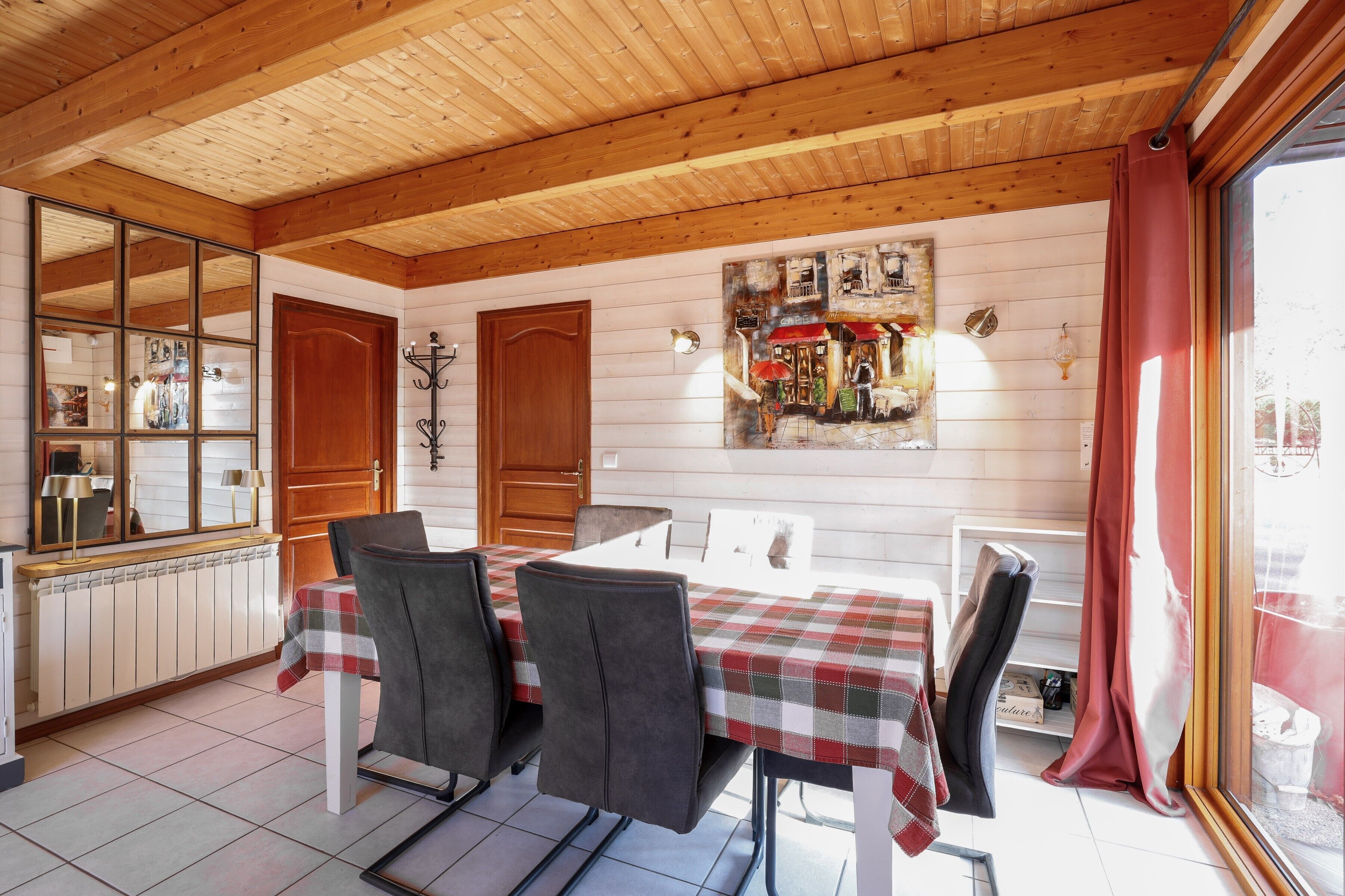 Een eetgedeelte met een houten plafond, een tafel met een geruit tafelkleed en stoelen.