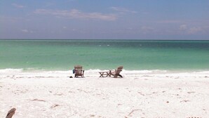 A beach with two wooden chairs and a table, a sandy beach, and a calm sea under a clear sky. - HVC #203 - Spa/Pool - Private Paradise on LBK! (Longboat Key)