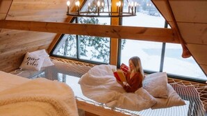 A cozy room with a bed, a window with a view of snow-covered trees, and a hanging light fixture. - The Water’s Edge * * Unique Muskoka Treehouse * * (Utterson)