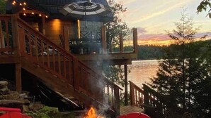 A wooden deck with a fire pit, overlooking a body of water. - The Water’s Edge * * Unique Muskoka Treehouse * * (Utterson)