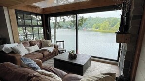 A living room with a leather sofa, a coffee table, and a large window overlooking a lake. - The Water’s Edge * * Unique Muskoka Treehouse * * (Utterson)
