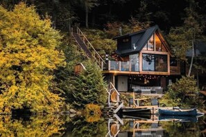A cabin with a glass facade, wooden deck, and a dock extending into a lake surrounded by trees.