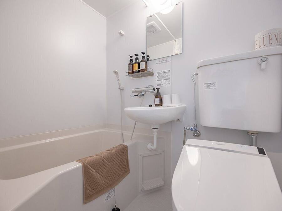 A modern bathroom with a bathtub, a sink, and a toilet. There are toiletries on a shelf and a towel hanging on the wall.