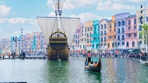 A historic ship in a canal with colorful buildings in the background. - Grand Central Hotel- Vinhomes Ocean Park 3 (Nghia Tru)