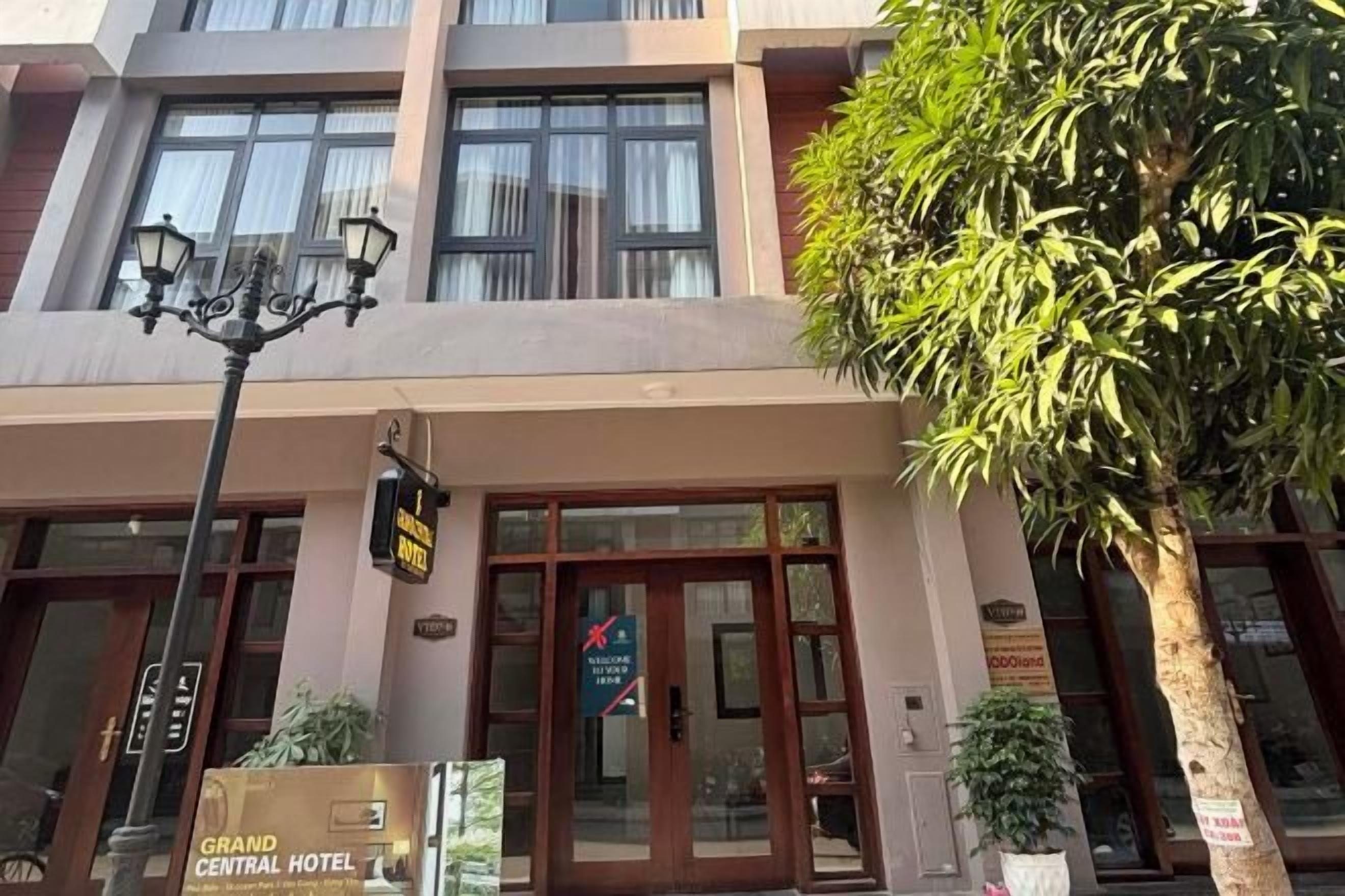 A hotel entrance with a sign, a street lamp, and a large tree.