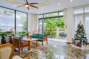 A spacious living area with a ceiling fan, large windows, a Christmas tree, and a view of the outdoors.
