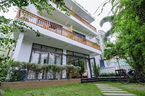 Un edifici residencial de diverses plantes amb balcons, un vestíbul cobert i un jardí ben cuidat.