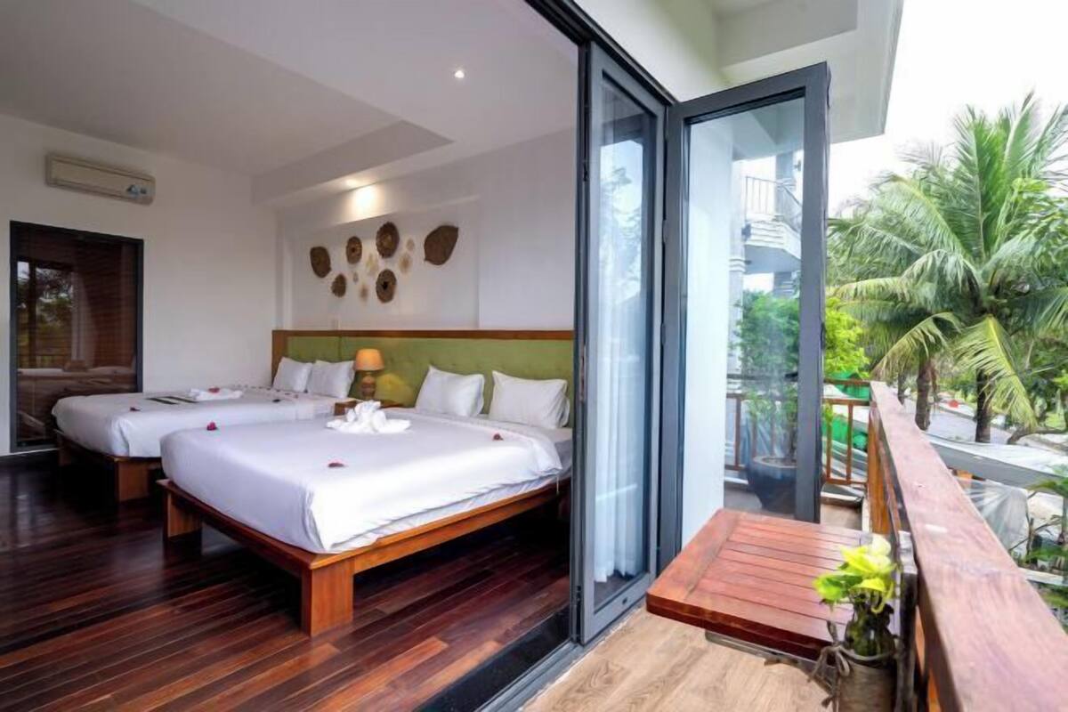 Ein modernes Hotelzimmer mit zwei Betten, einem Balkon mit Holzdeck und Blick auf Palmen.