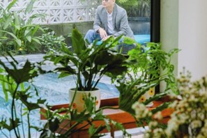 A person seated on a red bench in a room with a glass table, surrounded by potted plants. - Palm Riverside Boutique (Hoi An)