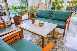 A room with a green sofa, wooden chairs, a table, and a bookshelf. - Palm Riverside Boutique (Hoi An)