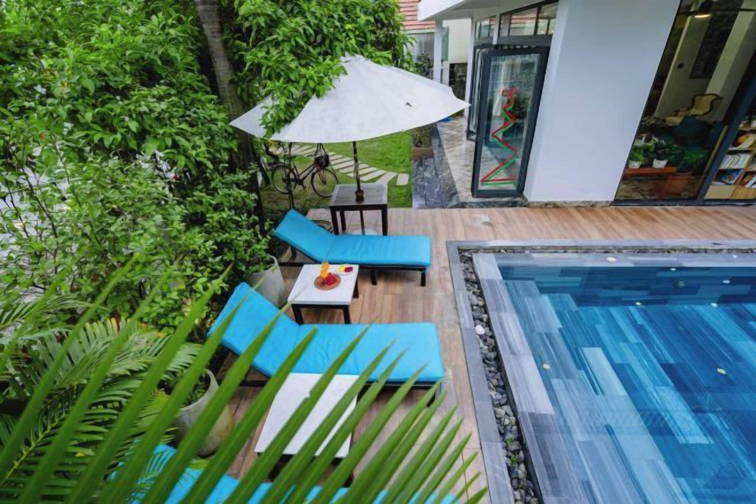 A poolside area with blue lounge chairs, a table with a drink, and an umbrella.