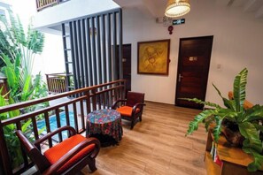Un hall d’hôtel avec un plancher en bois, une table ronde entourée de chaises, une rambarde et une porte.
