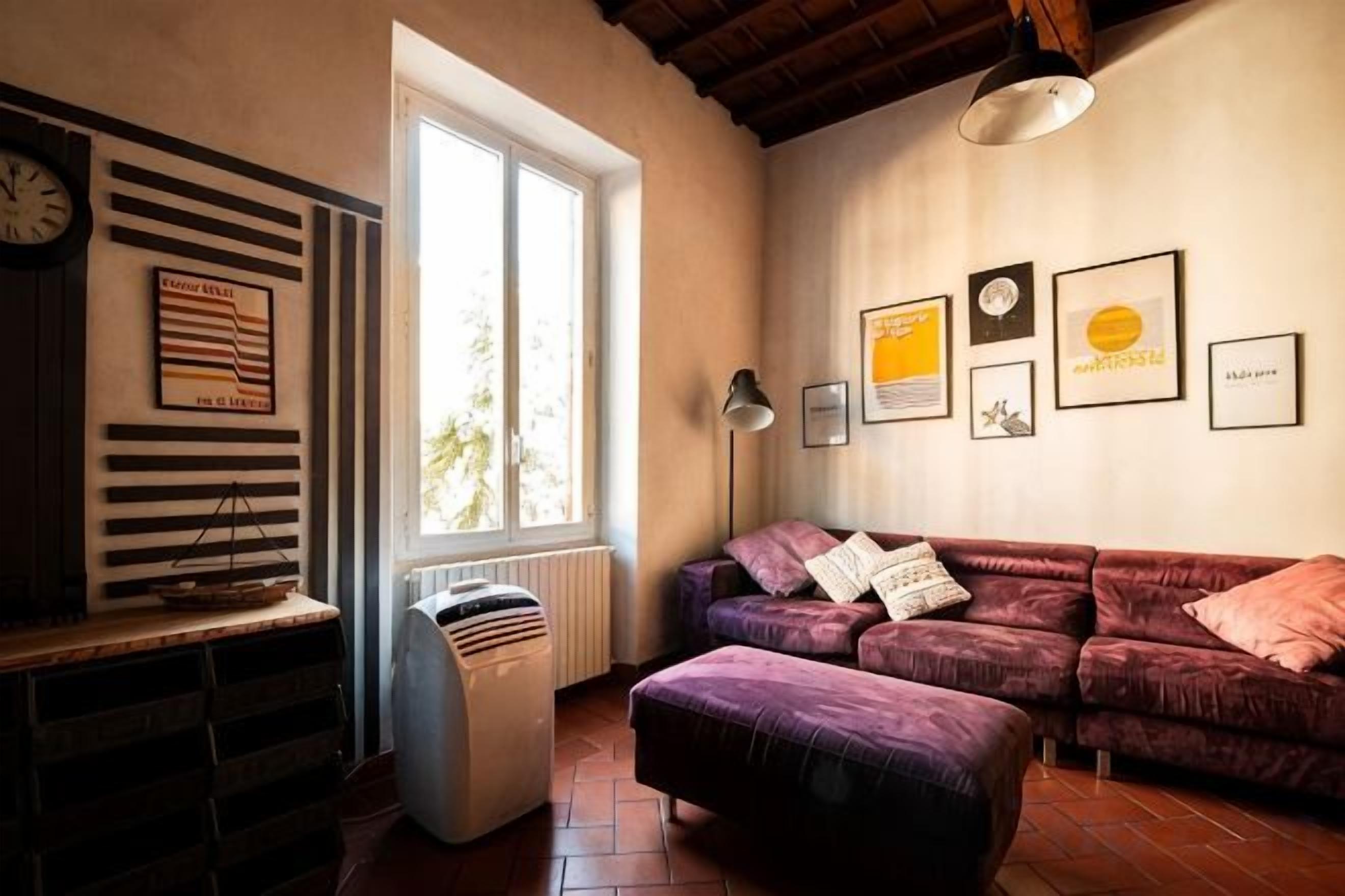 A living room with a sofa, a radiator, a window, and framed pictures on the wall.