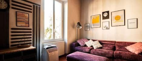 A living room with a sofa, a radiator, a window, and framed pictures on the wall.