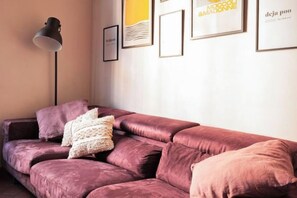 Ein Zimmer mit einer Couch, einer Stehlampe und gerahmten Kunstwerken an der Wand.