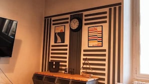 A room with a wall-mounted clock, a television, and a shelf with books and a decorative item. - Designer Apartments in Florence (Florence)