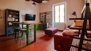 A room with a dining table, chairs, a television, a window, and a radiator. - Designer Apartments in Florence (Florence)