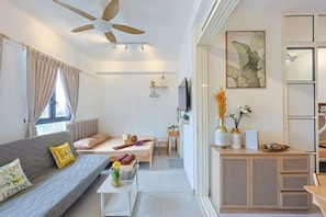 Una habitación moderna y luminosa con sofá, cama, televisor y un mueble con objetos decorativos.