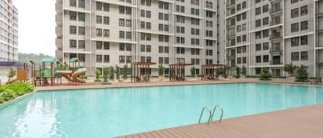 A swimming pool with a wooden deck, surrounded by high-rise residential buildings.