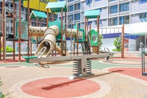 A playground with a slide and swings, set against a building with a blue awning.