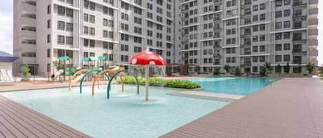 Un edificio residencial con piscina, parque infantil y una sombrilla roja.