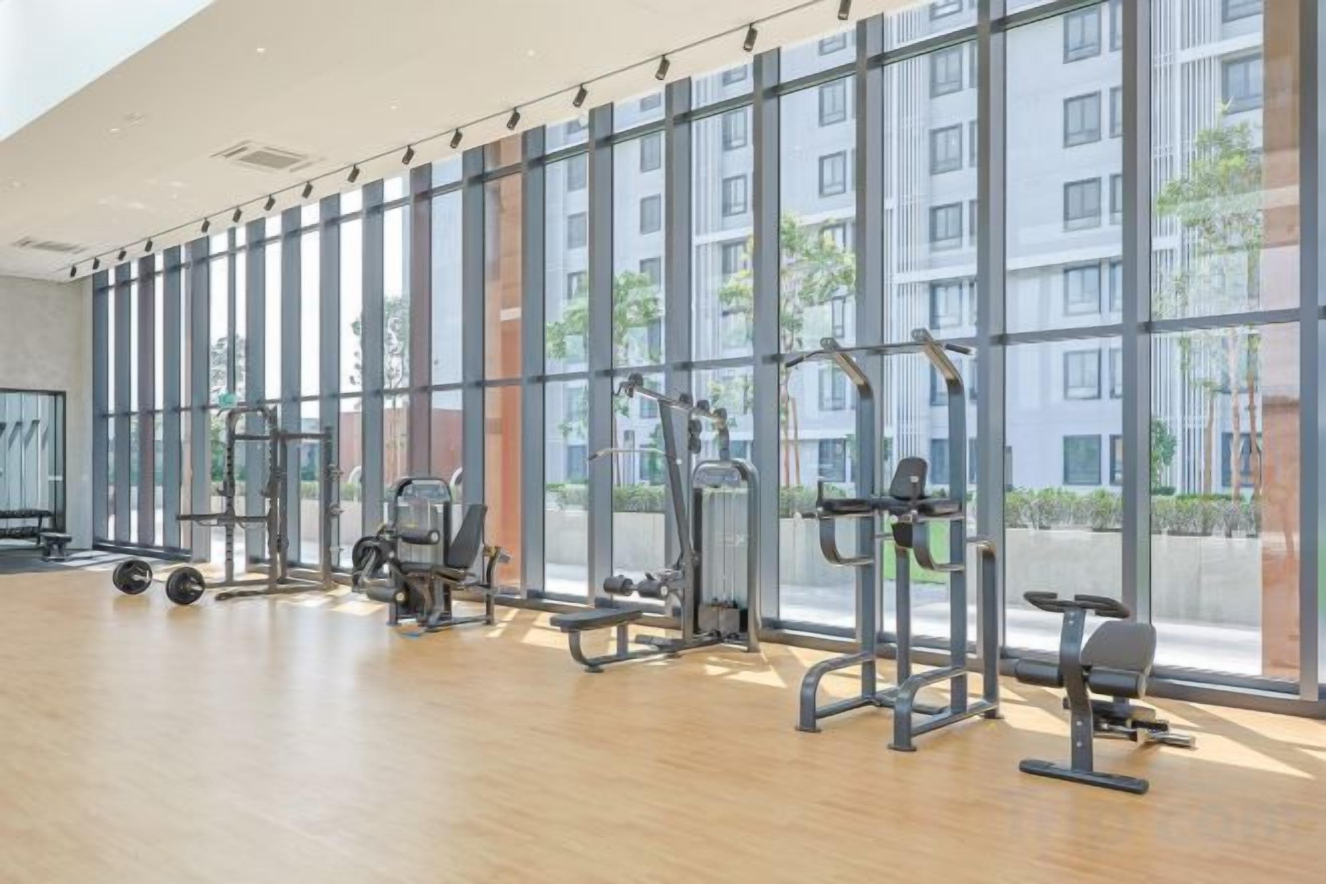 A gym with exercise equipment, large windows, and a wooden floor.