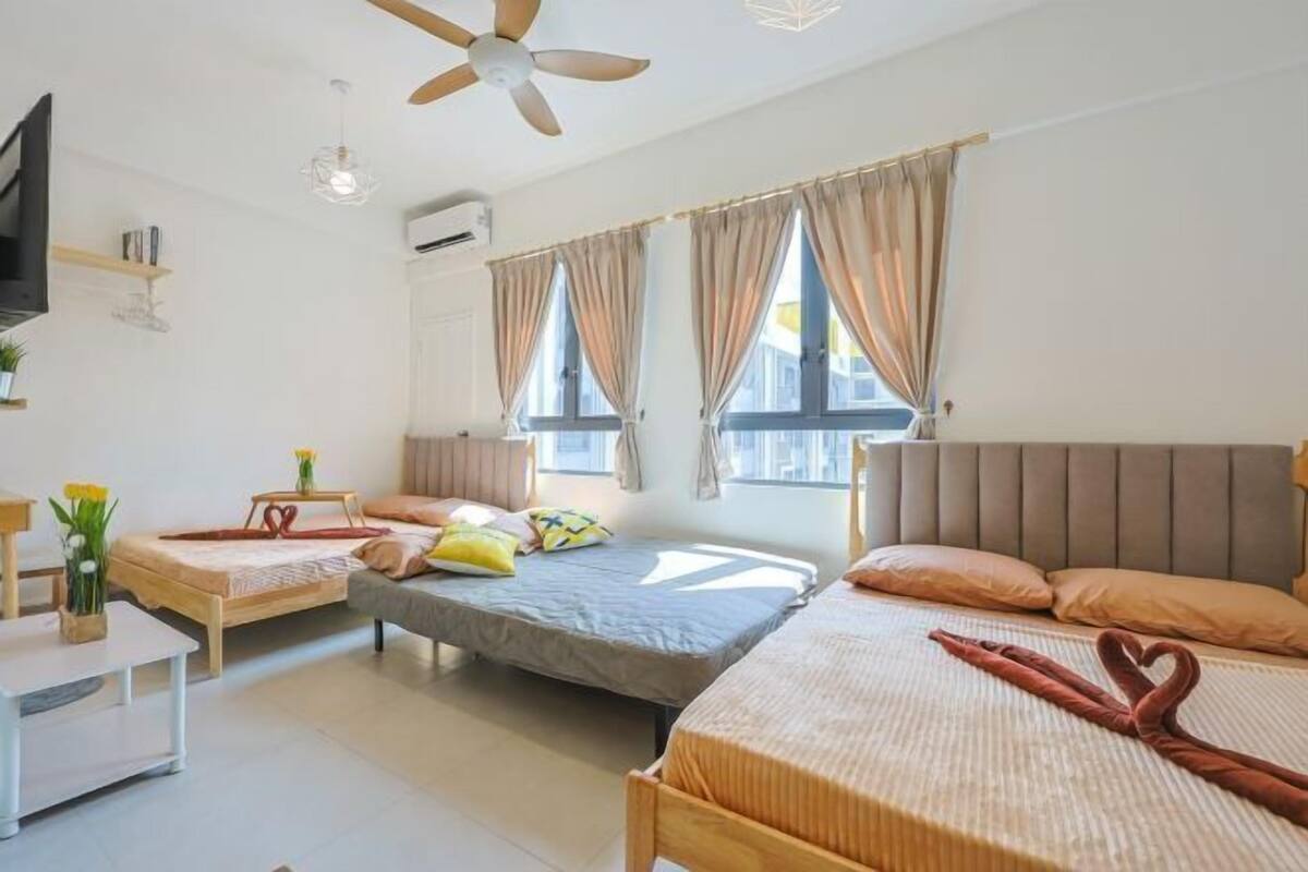 Une chambre d’hôtel avec deux lits, un ventilateur de plafond, une télévision et une petite table sur laquelle est posé un vase de fleurs.