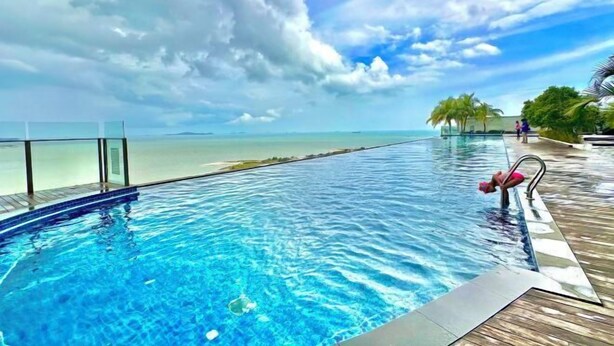 An infinity pool with a clear view of the ocean and a wooden deck. - Silverscape Residence Sea View Melaka by Stayrene (Melaka)