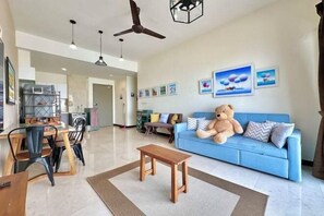 A living room with a blue sofa, a large teddy bear, a wooden coffee table, and ceiling fans. - Silverscape Residence Sea View Melaka by Stayrene (Melaka)