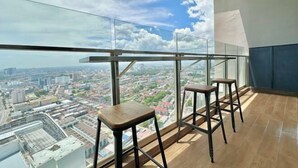 A high-rise balcony with a city view, two wooden stools, and a glass railing. - Silverscape Residence Sea View Melaka by Stayrene (Melaka)