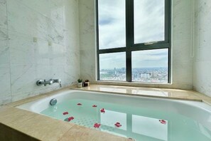 Une salle de bain avec une baignoire, une fenêtre donnant sur la ville et un mur en marbre.
