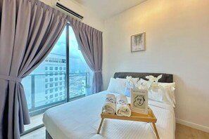 A hotel room with a large bed, a window with curtains, a bedside table with towels and a book, and a framed picture on the wall. - Silverscape Residence Sea View Melaka by Stayrene (Melaka)