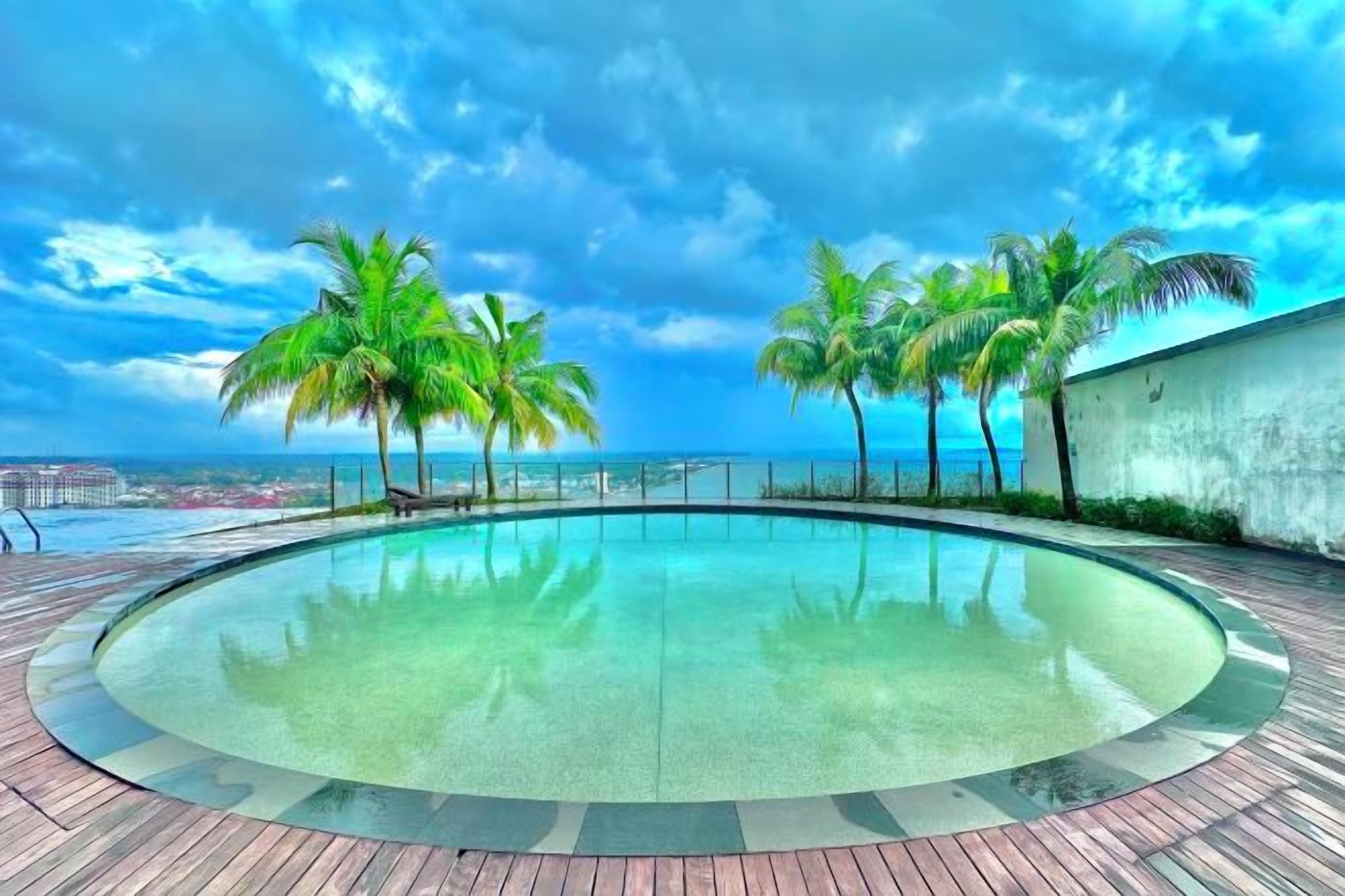 Ein kreisförmiger Infinity-Pool mit freiem Blick auf das Meer und Palmen.